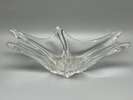 DEMI CRISTAL - Centro de mesa ou fruteira em vidro espesso transparente, apresentando design orgânico e fluido com bordas onduladas e pontiagudas de formato assimétrico, corpo com nervuras em relevo e base poligonal. Medindo 9x24x12 cm, a peça encontra-se em excelente estado de conservação, com desgastes naturais do tempo e marcas de uso.