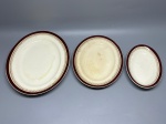 FAIANÇA - Conjunto de três peças em faiança inglesa da marca Alfred Meakin, composto por travessa e pratos ovais com fundo em tom creme, abas decoradas com faixa bordô e friso dourado com motivos estilizados. O lote inclui peças com medidas variando da maior com aproximadamente 32x24 cm até a menor com 21x13 cm. Todas contam com marcação no verso, exibindo o tradicional efeito craquelê da pasta cerâmica, além de desgastes naturais do tempo, manchas e marcas de uso.