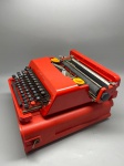 COLECIONISMO - Máquina de escrever portátil Olivetti Valentine vermelha, icônico design projetado por Ettore Sottsass e Perry King em 1969, acompanhada de sua maleta de transporte original integrada. A peça mede aproximadamente 11 x 35 x 13 cm, encontrando-se em bom estado geral de conservação, com marcas de uso e do tempo. Com perdas na alça.