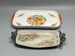 PORCELANA - Lote composto por: Bandeja retangular de cerâmica com fundo branco, estampa floral colorida em tons de laranja e verde, alças vermelhas e marca "Ars Bohemia" no verso, medindo 28x17 cm. Bandeja decorativa retangular com pintura à mão de rosas e flores azuis assinada por Roselle (Brasil, 1980), equipada com alças laterais em metal trabalhado, medindo 25x10 cm.