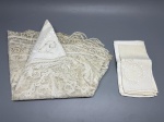 CAMA - MESA - BANHO - Lote composto por toalha oval (90x100 cm) em renda artesanal com ricos motivos florais e arabescos sobre fundo em rede geométrica, acompanhada de quatro guardanapos coordenados em tecido fino com bordados richelieu e recortes ajourados. As peças apresentam marcas do tempo e manchas amareladas de guarda.