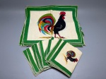 CAMA - MESA - BANHO - Lote composto por jogo americano com peças em tecido leve, decoradas com estampa de galo colorida em destaque e emolduradas por bordas verdes. O conjunto inclui peças de tamanhos diferentes, medindo 40x35 cm e 26x34 cm, apresentando marcas do tempo e manchas amareladas de guarda.