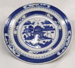 China / BLUE CANTON. Prato Macau ou Pagode em porcelana Jingdezhen de pasta dura. Esmalte azul e branco underglaze. Clássico design de Wu-tong Chinese parasol tree, paisagem de montanha, rio, pontes e pagodes. Diâmetro 15 cm. Marca de 7 caracteres chineses no verso. Excelente estado de conservação