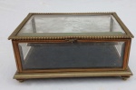 Caixa Vitrine montada em metal dourado, com placas em cristal bisotadas, placa de cima está com quebrados nas pontas, dobradiça ta tampa precisando ser soldada. Medidas: Alt. 14 x C. 29 x L. 22 cm.