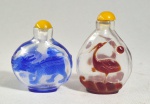 CHINA, DINASTIA QING, SÉC.XIX/XX - Dois antigos snuffs bottles sendo um em Peking glass de  vidro vermelho overlay, decorado com garça, ondas e sol, med. 7 cm, e outro, em vidro com overlay azul, decorado com animal mítico, med. 6.5 cm. com pq. trinco