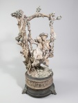 GIUSEPPE ARMANI - Grande escultura em resina italiana representando casal no balanço e flores, assinado, base em metal com caixa de música (travada). Pés cinzelados no formato de figuras. Med.: 45 x 23 cm.