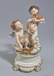 CAPODIMONTE - ITÁLIA - Delicadíssima escultura em porcelana tipo biscuit representando dois Anjinhos com ramos de flores. Marca azul na base. Discreto restauro. Med. 16 cm