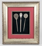 Quadro vitrine com 3 antigos prendedores chineses para cabelo em prata cinzelada, ditos 'HAIR PIN' (teor não identificado), Séc.XIX/XX, acomodados em moldura chinesa original em madeira com pátina dourada, envidraçada e com etiqueta. Medindo 20 cm o maior. Moldura: 41 x 36 cm.