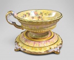 Rara xícara de chá com pires alto, estilo Vitoriano, feita em faiança policromada, reflexos furtacor sobre fundo amarelo e decorada com flores. Detalhes dourados. Possivelmente inglesa. Sem marca. Item de coleção. Med. 13.5 x 8 x 12.5 cm.