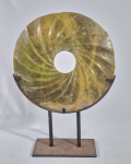 Raro e grande disco chinês em jade nefrita verde, no estilo arcaico, chamado "BI DISC", esculpido em formato espiralado XUANWEN, acomodado sobre estrutura de ferro. Bordas com desgastes irregulares. Superfície com calcificações e oxidações do tempo. Características do design indicam final do Período dos Reinos Combatentes ao início da Dinastia Han Ocidental (séculos III a I aC); podendo ser uma releitura nobre da Dinastia Ming ou Qing inicial. Med. 38 cm de altura  e 27 cm. Discos BI são originários do período Neolithico (circa 3300-2200 A.C) durante a Cultura Liangzhu, no delta do Rio Yangtze. Por causa do seu tamanho monumental de 27 centímetros, esses discos eram os símbolos máximos de prestígio político e aristocrático na China antiga. Eles eram usados pela nobreza em rituais importantes de adoração celeste e também eram colocados nos túmulos de governantes para guiar a alma da elite em direção à imortalidade.  ---- Ver na CHRISTIES E SOTHEBYS --  https://www.christies.com/en/search?entry=JAde%20bi%20disc&page=3&sortby=relevance&tab=sold_lots   ------- https://www.sothebys.com/en/search?query=jade+bi+disc&pfilters.dateRange=past  ----https://www.benjanssens.com/portfolio/jade-bi-disc-with-rice-grain-pattern/ ---- https://asia-archive.si.edu/learn/ancient-chinese-jades/liangzhu-jade-bi/