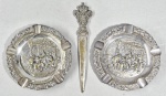 Lote com dois antigos cinzeiros em metal com cenas em relevo e um abridor de cartas com o brasão do Império Português. Banho com desgastes de uso. Med. 16 e 22 cm.