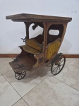 Miniatura decorativa de carruagem antiga em madeira entalhada, com estofamento em capitonê de veludo mostarda, rodas metálicas raiadas e detalhes ornamentais em ferro fundido. Medindo 60cm x 39cm x 70cm de altura. Peça necessita de reparos.