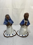 Par de esculturas em cerâmica vitrificada de estilo figurativo representando figuras religiosas em posição de oração com acabamento nas cores azul e branco sobre terracota. Medindo o maior 23cm de altura, com restauro.