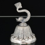METAL PRATEADO, uma (1) sineta de mão com campanula relevada em folhas, pega no formato de dolphin, pequenas mossas, medindo 9,5 cm altura, vide foto.
