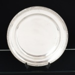 METAL PRATEADO, uma (1) travessa circular, ornamentação no padrão Império Napoleônico com borda reforçada e relevada em frisos intercalados por tracejados e flores, marca WOLFF (tradição desde 1894), medindo 33 cm diâmetro, vide foto.