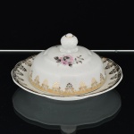 PORCELANA, uma (1) manteigueira com tampa e presentoir acoplado, ornada com rosa em policromia, barrado vegetalista a ouro, marca SCHMIDT (Pomerode, SC; Mauá, SP; Campo Largo, PR, fundada em 1945, ainda em atividade, maior fábrica de porcelana da América Latina), medindo 15,5 cm diâmetro, vide foto.