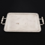 METAL PRATEADO, uma (1) bandeja retangular, ornamentação no padrão Império Napoleônico com frisos intercalados por X, alças em fumo de rolo, fundo liso, marca WOLFF (tradição desde 1894), medindo 42 x 33 cm mais as alças, vide foto.