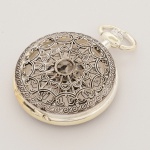 RELÓGIO, um (1) de algibeira (bolso), CÓPIA de relógio antigo, mostrador com algarismos romanos e visor, caixa com duas tampas a da frente em gradil vazado tipo mandala a traseira com visor, medindo 46 mm diâmetro, mecanismo a corda, funcionando e sem garantia, vide foto.