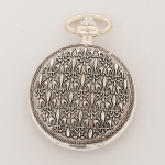 RELÓGIO, um (1) de algibeira (bolso), CÓPIA de relógio antigo, mostrador com algarismos arábicos, fase de lua (fake) e visor, além da legenda QUEBEC, caixa em metal prateado com duas tampas relevadas em flor de lis, medindo 46 mm diâmetro, mecanismo a corda, funcionando e sem garantia, vide foto.