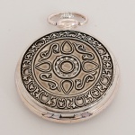 RELÓGIO, um (1) de algibeira (bolso), CÓPIA de relógio antigo, mostrador com algarismos romanos e visor, caixa em metal prateado com duas tampas relevadas em elementos vegetalistas, medindo 50 mm diâmetro, mecanismo a corda, funcionando e sem garantia, vide foto.