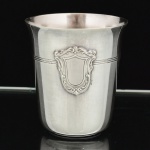 METAL PRATEADO, um (1) copo ligeiramente obcônico, ornado com escudo e frisos, marca de punções não identificados, medindo 6,5 cm altura e 5,5 cm diâmetro, vide foto.