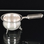 METAL PRATEADO, um (1) coador individual para infusão de chá, base trípode, borda serrilhada, medindo 6 cm diâmetro mais o cabo, sem marca de manufatura aparente, vide foto.