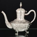 METAL PRATEADO, um (1) bule para café, ornamentação martelada e relevada em elementos vegetalistas, puncionada com a legenda MEXICANA encimada por sombreiro, pés de garra, medindo 22 cm altura, vide foto.