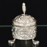 METAL PRATEADO, um (1) açucareiro com tampa, ornamentação martelada e relevada em elementos vegetalistas, puncionada com a legenda MEXICANA, pés de garra, recipiente interno em vidro, medindo 12 cm altura, vide foto.