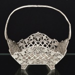 METAL PRATEADO, uma (1) fruteira no formato de cesta, vazada em pérgulas e parras, pés relevados em folhas com terminações macetadas, sem marca de manufatura aparente, medindo 18,5 x 19,5 x 18 cm, vide foto.