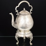 METAL PRATEADO, um (1) antigo samovar, bojo relevado em molduras, volutas e elementos vegetalistas, tampa encimada por elementos vegetalistas, alça com terminação em volutas e sinais de restauro, bico relevado em frisos, volutas e elementos vegetalistas, base trípode relevada em volutas e perolados com terminações em garra, gradil vazado, medindo 42 cm altura, vide foto.
