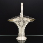 METAL PRATEADO, uma (1) fruteira de pé baixo no formato de cesta com alça, ornamentação relevada em escudos, perolados e elementos vegetalistas, acompanha recipiente em vidro, incolor e translúcido, sem marca de manufatura aparente, medindo 32 cm altura até a alça, vide foto.