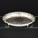 METAL PRATEADO, uma (1) bandeja circular com borda recortada e vazada em elementos vegetalistas, pés em esferas, sem marca de manufatura aparente, medindo 33 cm diâmetro, vide foto.