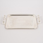 METAL PRATEADO, uma (1) bandeja retangular com quinas abauladas, fundo em baixo relevo com pérgulas, volutas e elementos vegetalistas, alças em fumo de rolo, sem marca de manufatura aparente, medindo 33 x 25,5 cm mais as alças, vide foto.