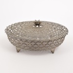 METAL PRATEADO, um (1) suporte com tampa para travessa circular, vazada, acabamento da tampa em flor, pés relevados em elementos vegetalistas, confeccionado em folha de flandres, ligeiros sinais de oxidação, medida interna 25 cm diâmetro, vide foto.
