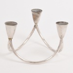 METAL PRATEADO, um (1) candelabro para três lumes, design contemporâneo, confeccionado em tubos cilíndricos vergados com terminações em bobeches, medindo aproximadamente 11 cm diâmetro e 8 cm altura, vide foto.