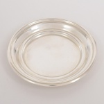 METAL PRATEADO, um (1) porta garrafa, liso, borda em degrau, sem marca de manufatura aparente, medindo 13,5 cm diâmetro, vide foto.