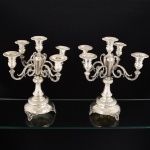 METAL PRATEADO, par (2) imponentes candelabros para cinco lumes cada, bobeches com barrados em folhas, haste central em colunetas sobrepostas com suporte para os outros lumes relevados em grifos, volutas e elementos vegetalistas, base quase cônica com pés relevados em conchas, volutas e elementos vegetalistas, sem marca de manufatura aparente, medindo 35 cm altura, vide foto.