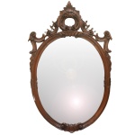 Espelho de parede de formato oval, com moldura em madeira lustrada, lavrada e ornada por frisos canelados, folhagens e volutas. Frontão ornamentado por vazados com arabescos, ramalhetes e lóbulos drapeados. 72 x 14 cm.