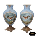 BACCARAT. France - Belíssimo par de vasos franceses em opalina azul lavanda, de formato piriforme. Bojos abaulados, ornamentados por delicadas reservas com pássaros em paisagens lacustres, emolduradas por volutas douradas e ramos floridos. Gargalos em corneta, decorados com pequenos arranjos florais. Versos realçados por ramalhetes em flor. Bases em bronze lavrado, adornadas por arabescos e sustentadas por pés vazados, revirados e inclinados. 46 x 24 cm.