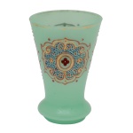 Copo em opalina verde água com realces a ouro. Base larga e achatada, encimada por bojo em corneta ornamentado por composições policromadas com molduras e volutas, centralizando medalhão com pequeno florão, intercaladas por adornos geométricos. Pé retraído, liso e circular. 13 x 8 cm.