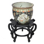 Aquário em porcelana chinesa policromada, de formato globular. Apresenta decoração com flores e pássaros em reservas, sobre fundo preto realçado por adornos florais e frisos estilizados. Borda rasa e revirada. Interior ornado por peixes e plantas aquáticas. Sob a base, marca apócrifa do reinado Qianlong. Acompanha base alta construída com hastes em madeira. O design é inspirado no estilo chinês tradicional, comumente utilizado como peça decorativa de interior. Acompanha base em madeira. 66 cm (MT). 33 x 38 cm (aquário).   34 x 49 cm (base).