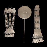 Conjunto de 3 adornos em metal espessurado a prata, da cultura Mapuche (povo indígena do Chile e Argentina),s endo: A) Grande pendente construído com 3 correntes de argolas, sustentando meia lua com moedas e encimado por par de aves estilizadas. (25 x 10 cm).B) Broche circular decorada em pontilhados, com círculos e cruz ao centro. (30 x 12 cm). C) Grande pendente vertical, montado com 5 placas reunidas por argolas, rematado na parte inferior por 6 pingentes. (32 x 7 cm). Acervo Particular MAVP.