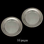 Conjunto com 10 pratos para pão em metal espessurado a prata. Apresenta formato circular com bordas ornamentadas. Manufatura Toledo, Indústria Argentina. 15 cm. Acervo Particular Maria Anna do Valle Pereira, SP.