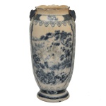 Vaso decorativo em cerâmica com pintura em tons de azul e branco, apresentando motivos de paisagem e acabamento detalhado na borda e na base. Corpo cilíndrico com alças ornamentais nas laterais superiores e borda superior ondulada ou recortada. 26 x 12 cm.