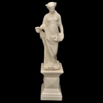 Escultura em cerâmica, de cor branca, representada por figura feminina, tendo na base a inscrição Outono.  A figura humana apresenta vestimentas drapeadas e está posicionado sobre um pedestal estilizado com detalhes geométricos. 128 cm (MT). 84 x 23 x 24 cm (escultura). 44 x 30 x 30 cm (base)