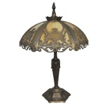 Luminária de mesa de estilo Art Nouveau feita de metal fundido patinado e fenestrado. Cúpula é composta por placas de vidro, iridescente em tom de marfim. Fuste e base apresentam elaborados detalhes em relevo, cinzelados com flores. 67 x 45 x 45 cm (MT). 30 x 45 cm (cúpula).
