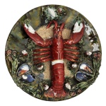 Medalhão decorativo em cerâmica portuguesa, da região de Caldas da Rainha, policromada e esmaltada, apresentando um lagostim central em relevo rodeado por outros mariscos e uma textura que lembra areia. 32 cm.