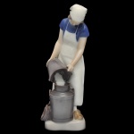 ROYAL COPENHAGEN. Bing & Grndahl. Artista Axel Locher. "Menina com Lata de Leite" - Estatueta em porcelana dinamarquesa exibindo um acabamento vidrado em tons pastel e suaves, típicos da marca (azul-cinzento, branco e marrom), retratando uma camponesa vestindo avental branco e blusa azul, despejando leite em um recipiente. No verso marca da manufatura Bing & Grndahl e modelo número 2181. 22 x 8 x 7 cm.