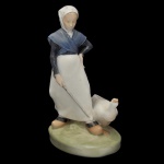 ROYAL COPENHAGEN. Artista Christian Thomsen. "Goose Girl" (Menina dos Gansos). Estatueta em porcelana dinamarquesa exibindo um acabamento vidrado em tons pastel e suaves, típicos da marca (azul-cinzento, branco e marrom). No verso marca da manufatura e o número do modelo 528. 20 x 11 x 8 cm.