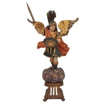 SÃO MIGUEL ARCANJO. Séc. XX - Escultura sacra esculpida em madeira policromada e dourada. A imagem aparece representado como o chefe das milícias celestes, vestindo trajes inspirados em um legionário romano (armadura e manto flutuante), ostentando grandes asas douradas, empunhando uma espada elevada e segurando um escudo circular. O arcanjo está posicionado sob uma nuvem estilizada, que por sua vez se apoia em um pedestal trabalhado. 64 x 36 x 17 cm.